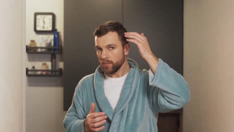 Close-up-portrait-of-a-handsome-man-in-a-bathrobe-examining-his-hair