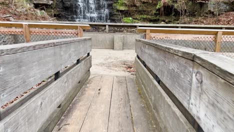 Zu-Fuß-über-Eine-Holzbrücke,-Die-Einen-Rauschenden-Blauen-Und-Kristallklaren-Wasserfall-Und-Einen-Teich-Im-Cove-Spring-Park-Frankfurt,-Kentucky,-In-4k-Slo-Mo-60fps-Enthüllt