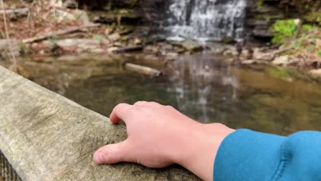slow-motion-clip-of-a-man-tapping-his-finger-on-a-wooden-railing-watching-a-beautiful-waterfall-in-cove-spring-park-frankfort-kentucky-usa-4k