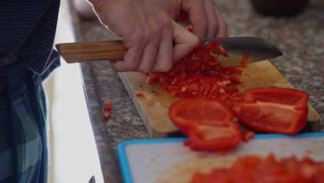 Close-up-man-cutting-red-pepper-on-wooden-board