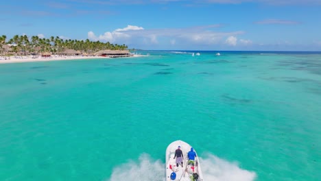 Speedboat-with-two-people-on-board-sailing-on-turquoise-ocean-waters-of-Playa-Blanca-beach,-Punta-Cana-in-Dominican-Republic