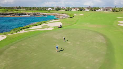 Luftaufnahme-Eines-Paares,-Das-Auf-Einem-Luxusgolfplatz-Golf-Spielt,-Mit-Karibischem-Meer-Im-Hintergrund
