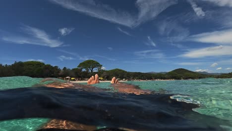 First-person-low-angle-pov-of-man-legs-and-feet-relaxing-while-floating-on-sea-water-at-Santa-Giulia-popular-beach-in-Corsica-island,-France