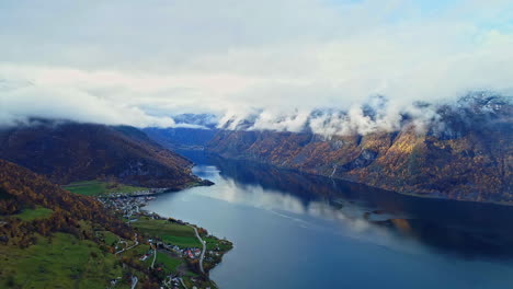 Hochwinkelaufnahme-Des-Wunderschönen-Norwegischen-Fjords-Mit-Blick-Auf-Eine-Stadt-Entlang-Der-Küste-In-Der-Ferne-An-Einem-Bewölkten-Tag