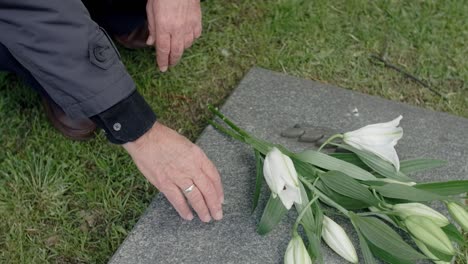 Formally-dressed-man-is-kneeling-down-at-the-grave-of-a-loved-one-to-put-down-flowers