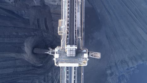Top-down-drone-shot-of-Coal-Mine-Plant,-Coal-coming-off-conveyor-belt-with-caterpillar-mining-trucks-moving-the-coal-around