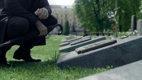 Formally-dressed-man-is-kneeling-down-at-the-grave-of-a-loved-one