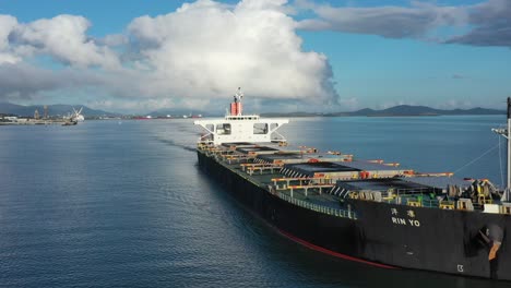 Drone-stationary-shot-of-Large-Coal-Ship-Leaving-Port,-Gladstone-Queensland-Australia