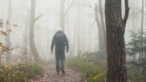Man-is-hiking-in-a-misty-forest,-fogy-atmosphere-during-autumn
