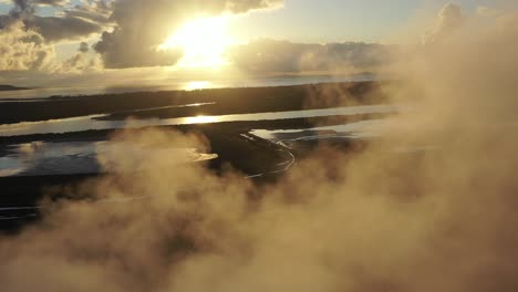 Drone-shot-revealing-coal-and-metal-factory-at-sunrise,-flying-through-large-steam-smoke-stacks-in-operation