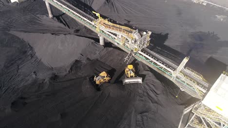 Drone-shot-of-Coal-Mine-Plant,-Coal-coming-off-conveyor-belt-with-caterpillar-mining-trucks-moving-the-coal-around