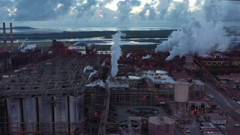 Drone-shot-of-coal-and-metal-factory-at-dawn,-large-steam-smoke-stacks-operating
