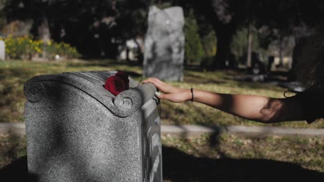 Woman-is-standing-in-front-of-thee-grave-of-a-loved-one-leaving-a-rose-behind