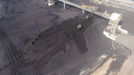 Aerial-drone-shot-of-Coal-Mine-Plant,-Coal-coming-off-conveyor-belt-with-caterpillar-mining-trucks-moving-the-coal-around