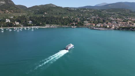 Aerial-shot-tracking-a-large-boat-approaching-the-coast-of-Garda,-Lake-Garda,-Italy
