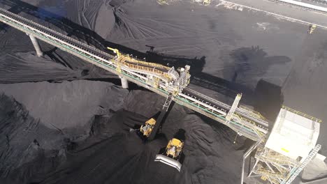 Drone-orbiting-shot-of-Coal-Mine-Plant,-Coal-coming-off-conveyor-belt-with-caterpillar-mining-trucks-moving-the-coal-around