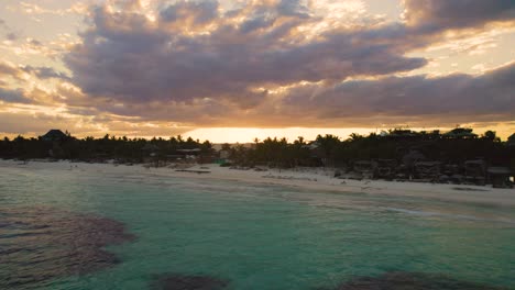 Aerial-view-over-Akiin-beach-in-Tulum,-Mexico-while-people-enjoy-the-sunset-on-the-beach