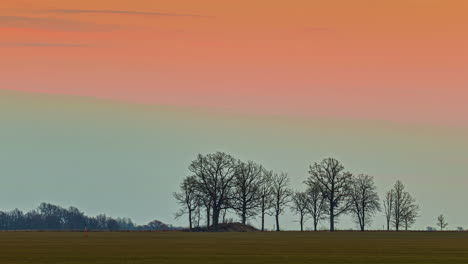 Timelapse-shot-of-a-huge-farmland-against-an-orange-sunset-sky-above-during-evening-time