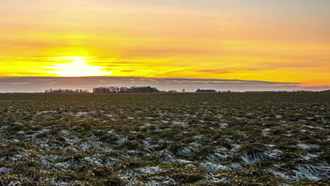 Harvested-farm-field-with-a-dusting-of-snow-and-a-bright,-golden-sunrise-time-lapse