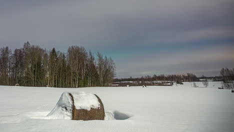 Timelapse-shot-of-white-cloud-movment-over-hay-bales-covered-with-snow-with-aurora-visible-in-the-background-at-daytime