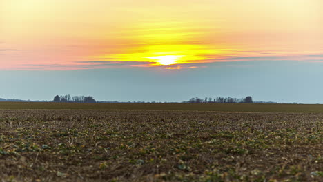 Bright-yellow-sunset-over-a-farmland-field-in-autumn---static-wide-angle-time-lapse