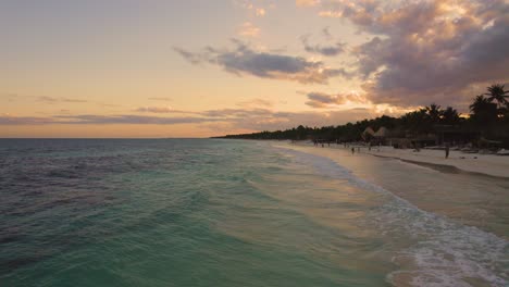 Aerial-view-close-to-the-the-carribean-ocean-at-the-Akiin-beach-in-Tulum,-Mexico-during-Sunset-with-people-enjoying-their-beach-holiday
