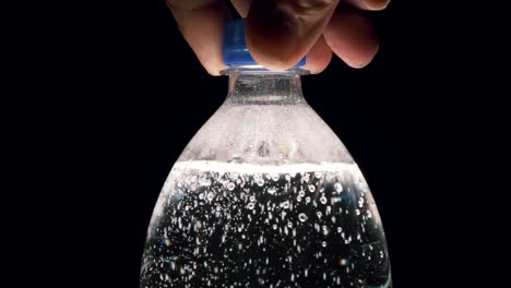 A-bottle-of-carbonated-water-is-unscrewed-by-hand-on-a-black-background