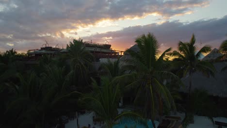 Luftaufnahme-Eines-Touristenkomplexes-Zwischen-Palmen-Bei-Einem-Wunderschönen-Sonnenuntergang