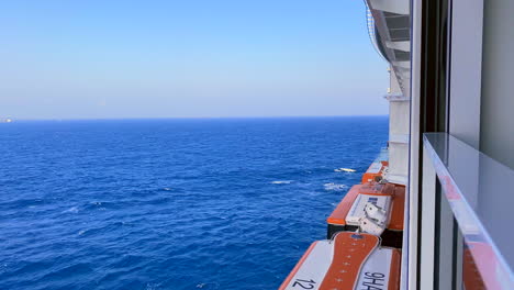 Cruise-ships-sailing-towards-horizon-view-from-balcony-and-lifeboats-below