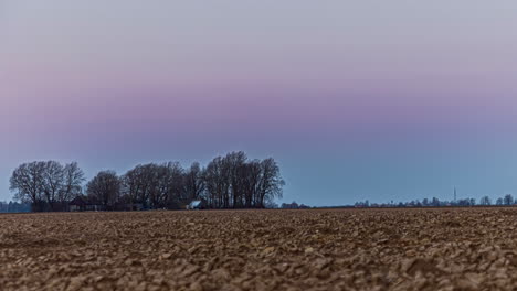 Timelapse-shot-over-brown-agricultural-farmland-during-evening-time-with-colorful-sky-after-sunset
