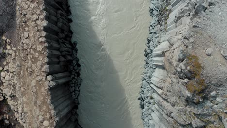 Drone-top-down-riser-reveals-basalt-columns,-glacial-river---Studlagil,-Iceland