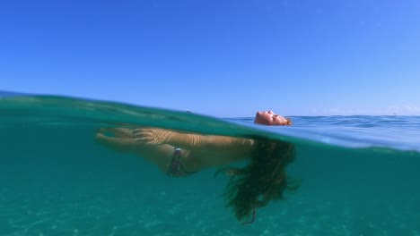 Halbe-Unterwasserszene-Eines-Kleinen-Mädchens-Mit-Langen-Haaren,-Das-Sich-Entspannt-Und-Im-Türkisfarbenen-Meerwasser-Schwimmt