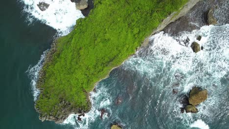 Aerial-view-of-lush-green-cliffs-and-waves-crashing-on-coral-rock-shore
