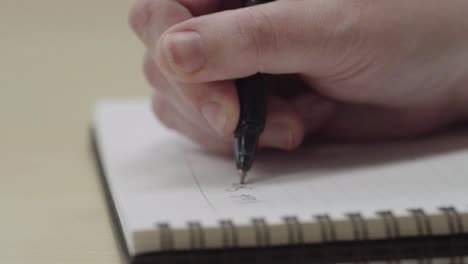 Close-up-of-anonymous-person's-hands-writing-on-a-notebook-with-a-pen-in-slow-motion
