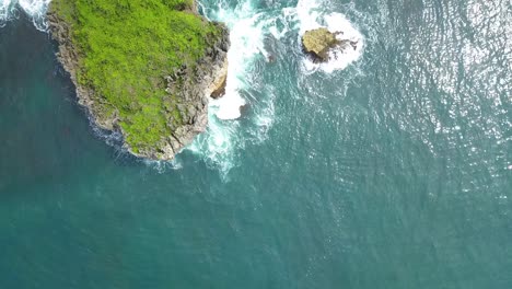 Overhead-drone-shot-of-sea-wave-crashing-against-coral-rock