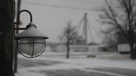 Vintage-looking-light-fixture-and-bulb-hands-on-the-side-of-old-building-in-a-small-midwest,-snow-covered-town-on-a-cold-winter-day-in-December-during-Christmas-time