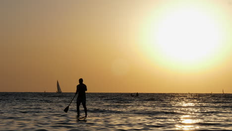 Man-In-Silhouette-Stand-up-Paddling-In-The-Sea-Against-Golden-Sun-In-The-Sky-In-Tel-Aviv,-Israel