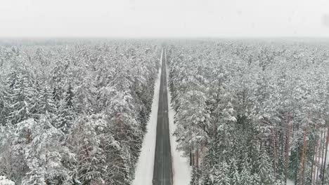 Endless-forest-road-in-forest-covered-in-snow-during-snowfall,-aerial-view
