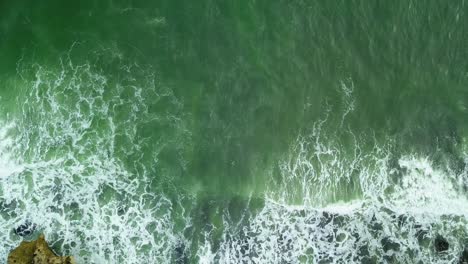 Top-view-of-turquoise-green-ocean-as-waves-break-on-rocks-on-coast-of-Indonesia