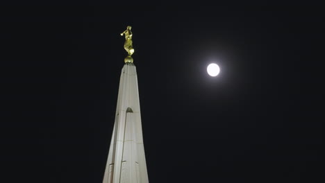 Statue-of-The-Angel-Moroni-on-Top-of-a-LDS-Mormon-Temple-Church-Building-at-Night-with-Moon-in-Gilbert,-Arizona