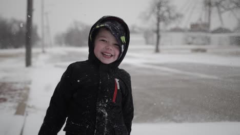 Young,-happy,-smiling-boy-wearing-a-coat-playing-outside-throws-snow-in-the-air-while-laughing-on-a-cold,-winter-day-in-December-during-Christmas-break-in-a-small-town-in-the-midwest