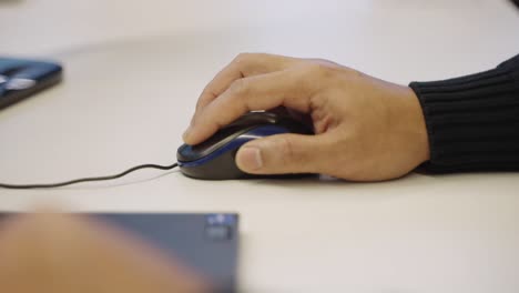 Close-up-of-anonymous-man's-hands-scrolling-mouse-wheel-next-to-laptop-in-an-office