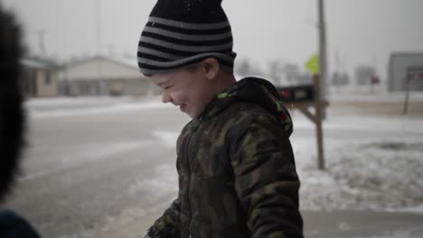 Niño-Parado-Afuera-En-La-Nieve-Sonríe-Mirando-La-Cámara-Durante-Las-Vacaciones-De-Navidad-En-Un-Pequeño-Pueblo-En-El-Medio-Oeste