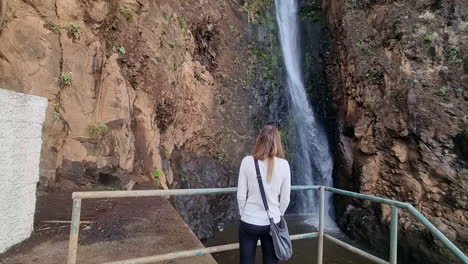 Cinematic-shot-of-a-woman-from-behind-admiring-the-waterfall-in-the-city-of-Paul-do-Mar-on-the-island-of-Madeira
