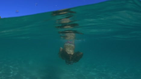 Halbe-Unterwasserszene-Eines-Kleinen-Mädchens-Mit-Taucherbrille,-Das-In-Klarem-Türkisfarbenem-Meerwasser-In-Richtung-Kamera-Schwimmt-Und-Meerwasser-Spritzt