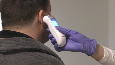 Nurse-Checking-Temperature-Of-Male-Patient-With-Digital-Thermometer-On-Ear