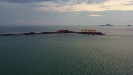 Aerial-drone-flyover-straits-of-malacca,-sea-in-west-coast-Malaysia-capturing-the-export-wharf-of-brazilian-vale-iron-ore-mining-corporation,-logistic-bulk-terminal-jetty-along-the-horizon-at-dusk