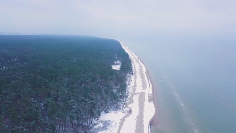 Beautiful-aerial-establishing-view-of-Baltic-sea-coast-on-a-overcast-winter-day,-beach-with-white-sand-covered-by-snow,-coastal-erosion,-climate-changes,-wide-angle-drone-shot-moving-forward