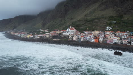 Fantastic-aerial-shot-over-the-coast-of-the-city-of-Paul-do-Mar,-on-the-island-of-Madeira,-where-you-can-see-the-waves-breaking-against-the-coast