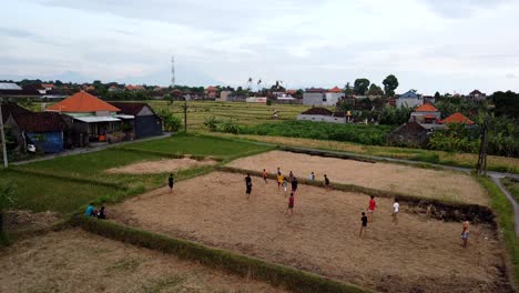 Boys-Play-Soccer-in-Rural-Field,-Indonesia,-Kids-Ball-Match-Aerial-Time-Lapse-in-Bali-Ricefield,-Countryside-in-Local-Area